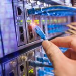 man working in network server room with fiber optic hub for digital communications and internet
